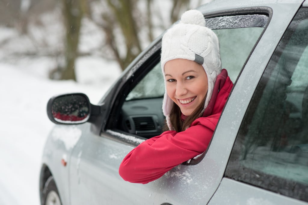 Image of smiling girl leaning out car window, took hat on, winter and snowy.