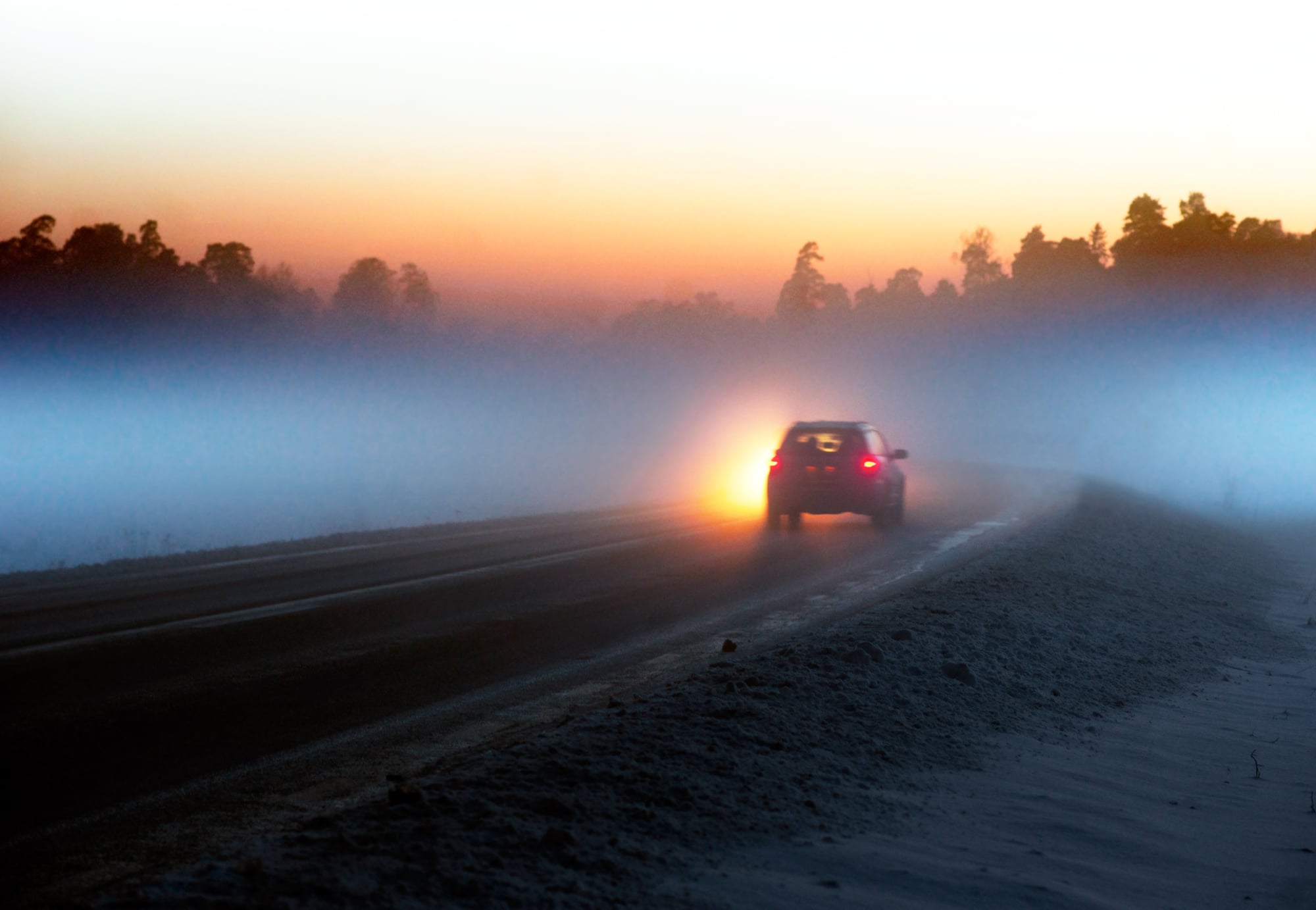 image of a car driving on wet foggy road toward sunset
