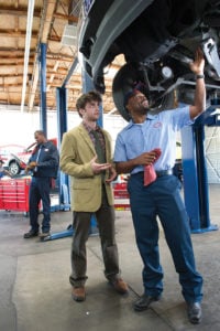 image of AAMCO mechanic and customer under car on lift, mechanic showing customer repairs needed.