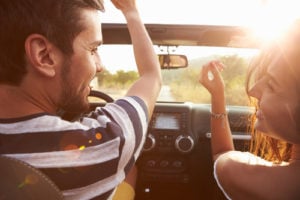 image of Young Couple Driving Along Country Road In Open Top Car