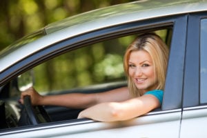 image of young woman smiling at us from driver side of car, open window.