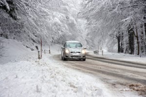 Car driving on a snowy winter road surrounded by trees