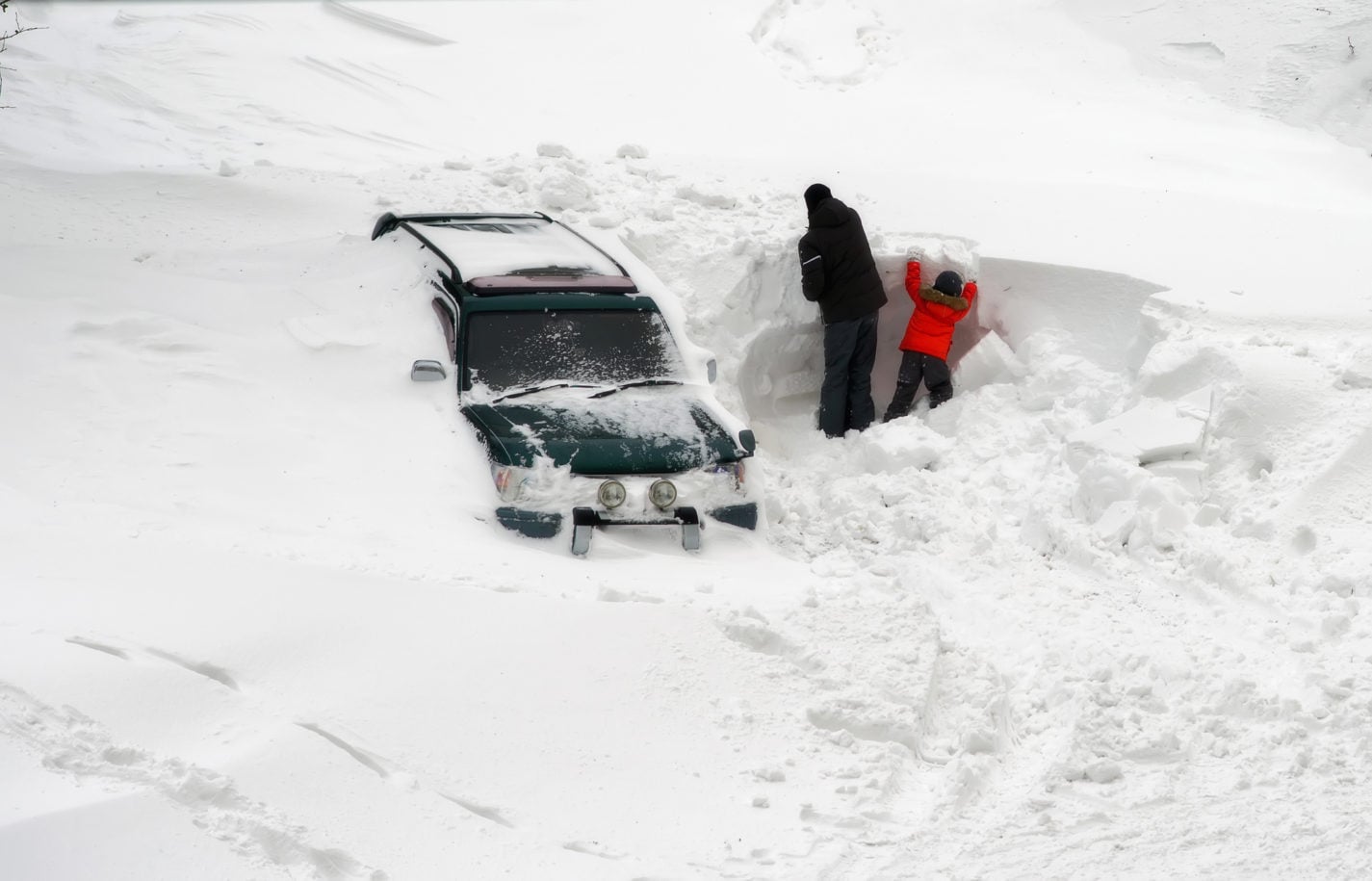 image of car hopelessly stuck in an avalanche of snow, but someone is trying to dig it out.