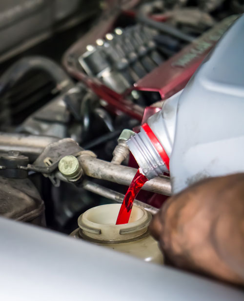 image of a person pouring red liquid into container under car hood